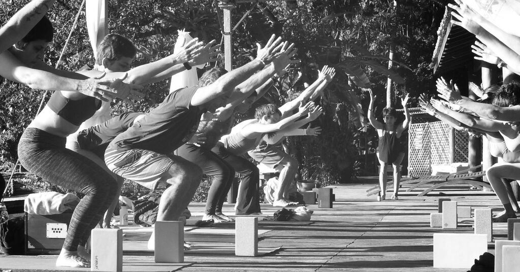 Em preto e branco: a turma inteira em utkaṭāsana, ao ar livre.