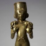 Estátua de latão da Caxemira do deus Sol Sūrya em pé, de túnica e botas, com olhos incrustados de prata